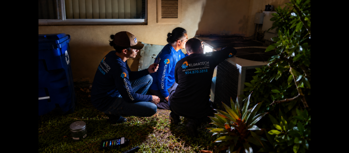 Three KlimaTech technicians working on an outdoor air conditioning unit at night.